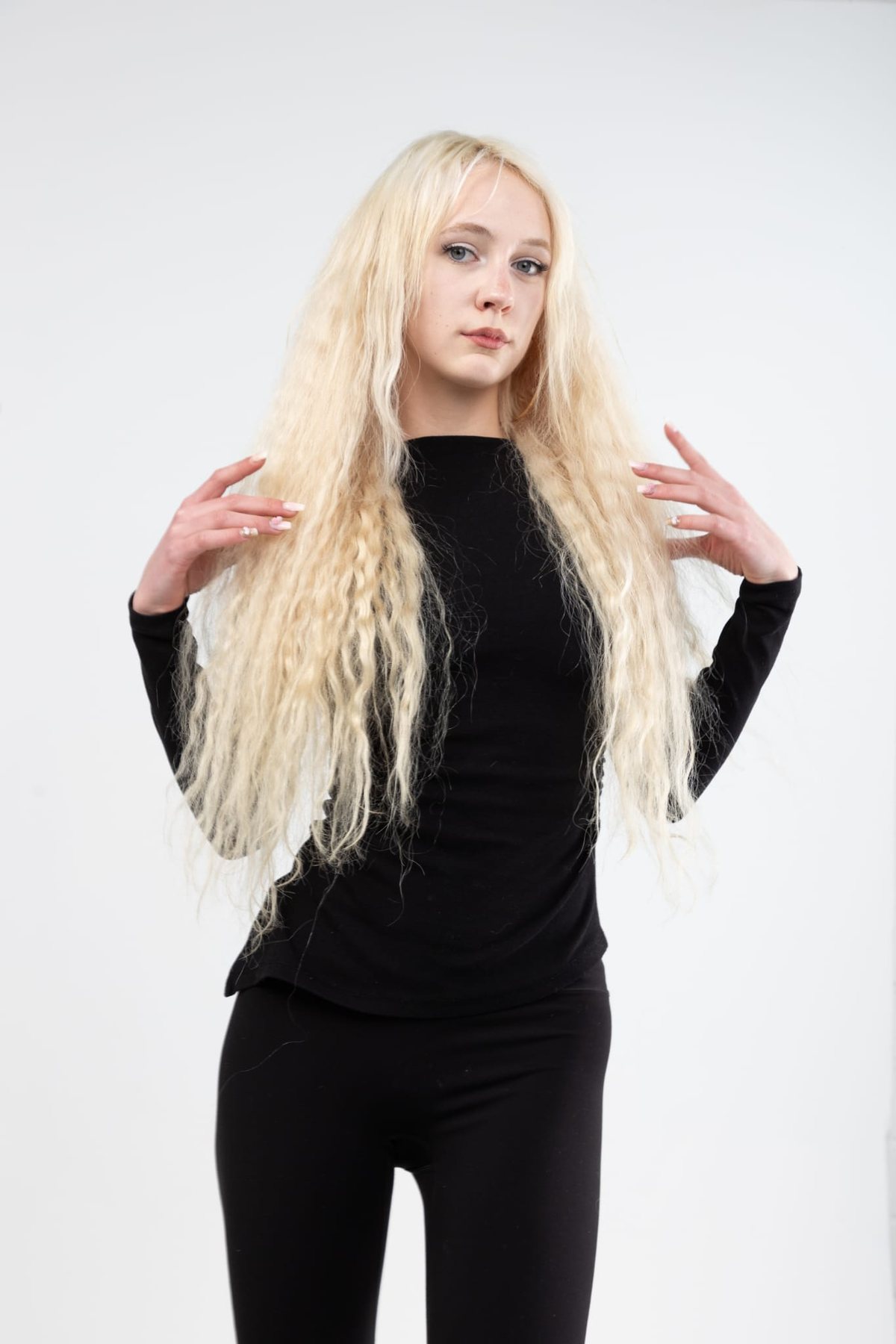 Model mit langen, gewellten blonden Haaren vor weißem Hintergrund